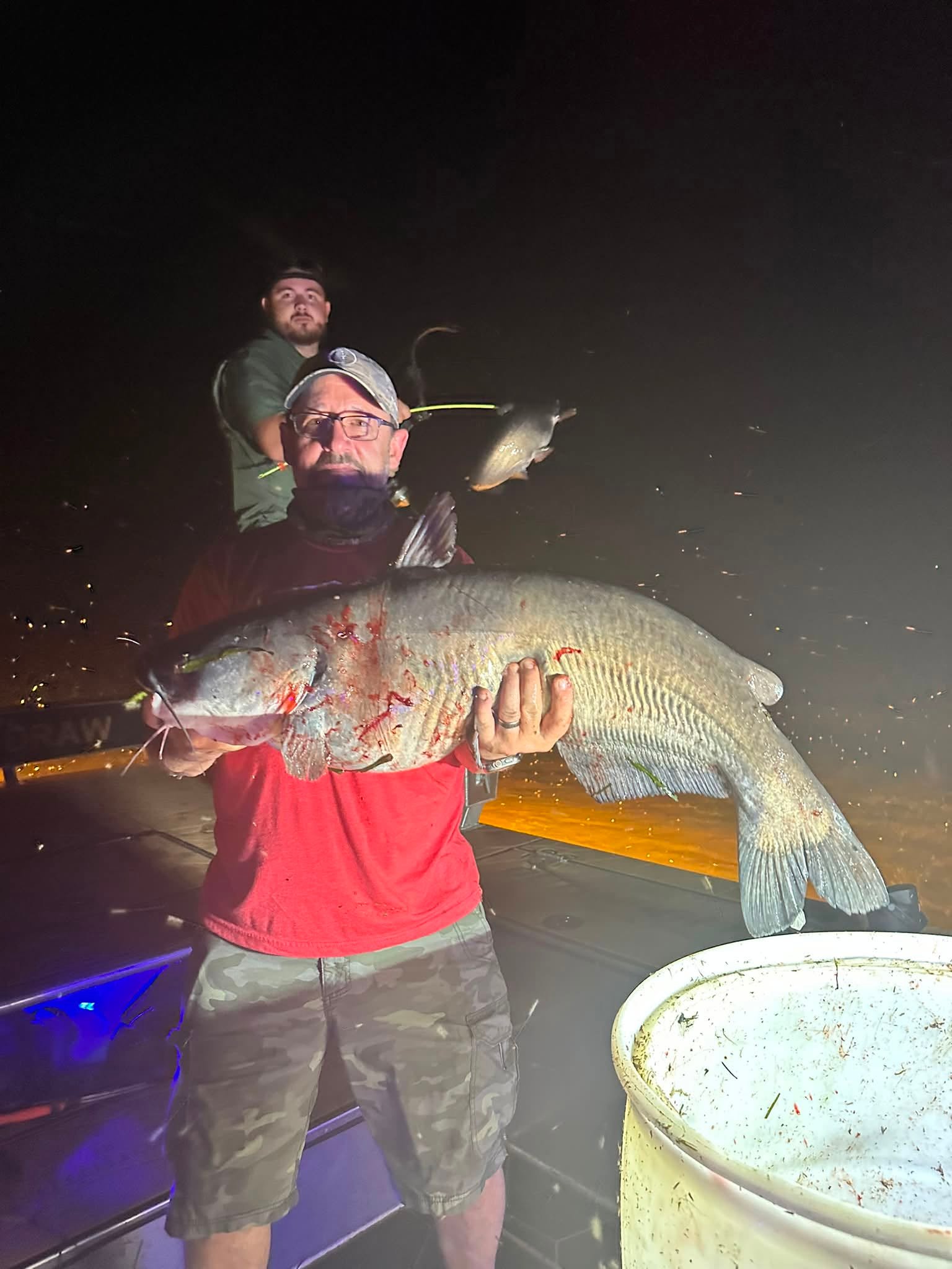 Angler holding a flathead catfish caught bowfishing at night