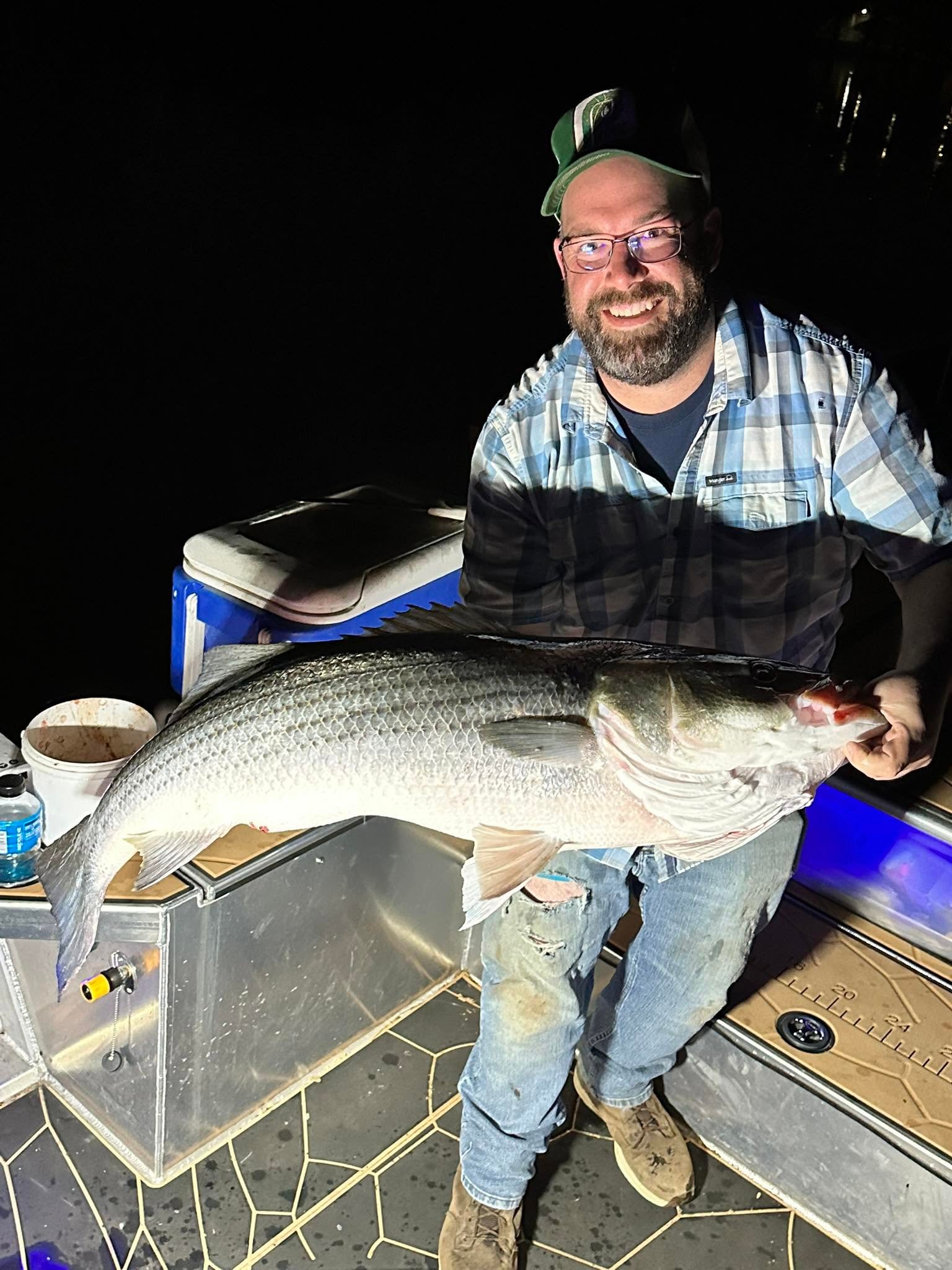 Angler holding a striped bass caught on the Delaware River at night
